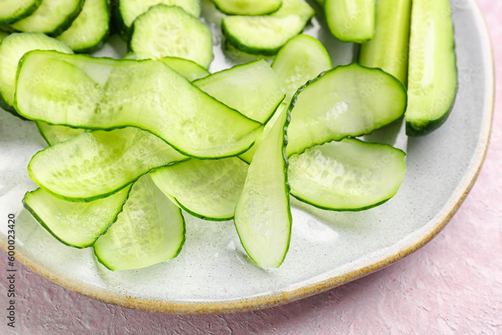 Plate with fresh cut cucumber on light background