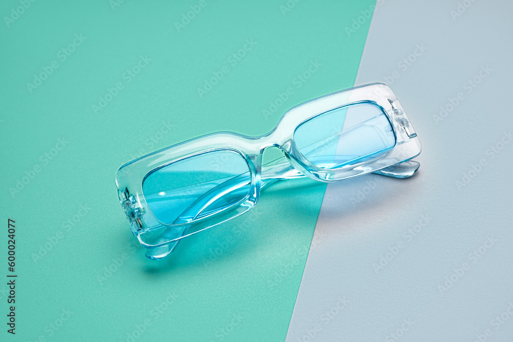 Stylish blue sunglasses on color background