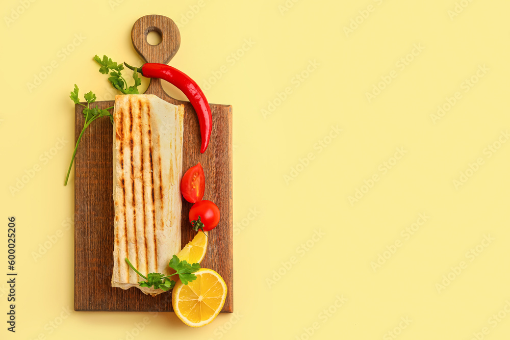 Board with tasty shawarma and ingredients on yellow background