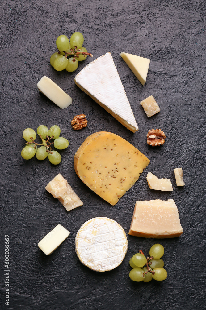 Different types of tasty cheese, nuts and grapes on dark background