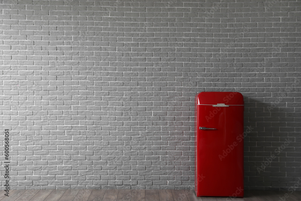 Stylish refrigerator near brick wall in kitchen