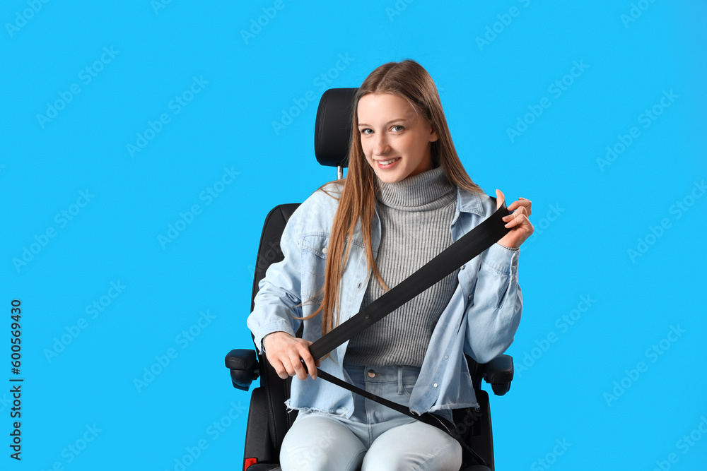 Female student fastened in car seat on blue background