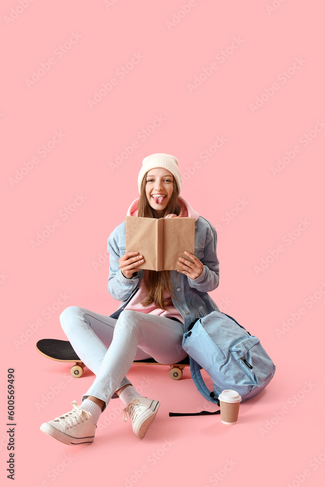 Female student with book showing tongue on pink background