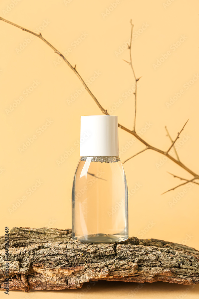 Bottle of micellar water with tree branch and bark on beige background, closeup