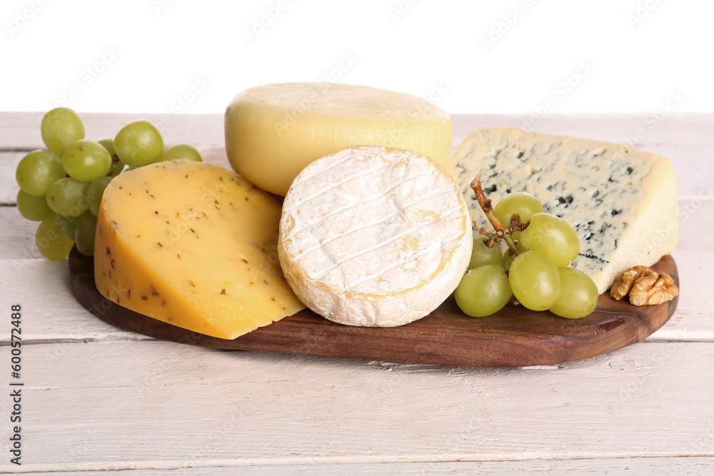 Wooden board with different types of tasty cheese and grapes on table against white background