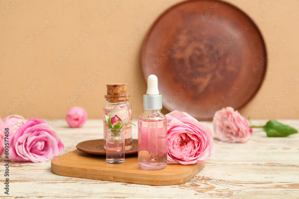 Bottles of cosmetic oil with rose extract and flowers on light wooden table