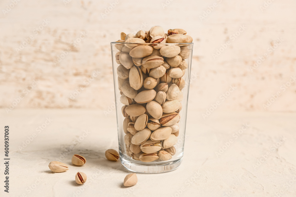 Glass with tasty pistachio nuts on beige table