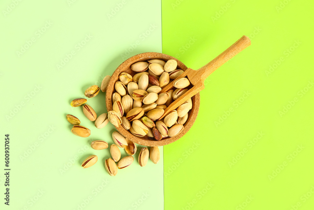 Wooden bowl with tasty pistachio nuts and scoop on green background