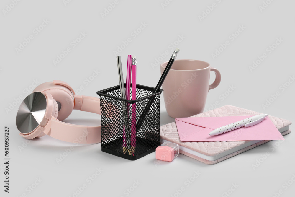 Stationery holder, notebook, headphones and cup on grey background