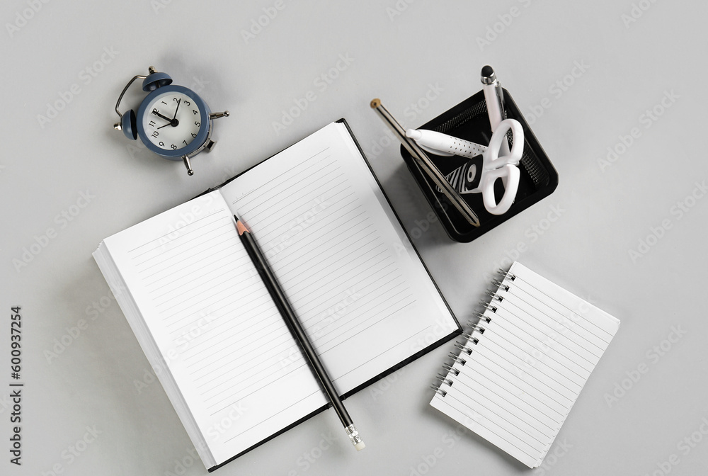 Stationery holder, notebooks and alarm on grey background