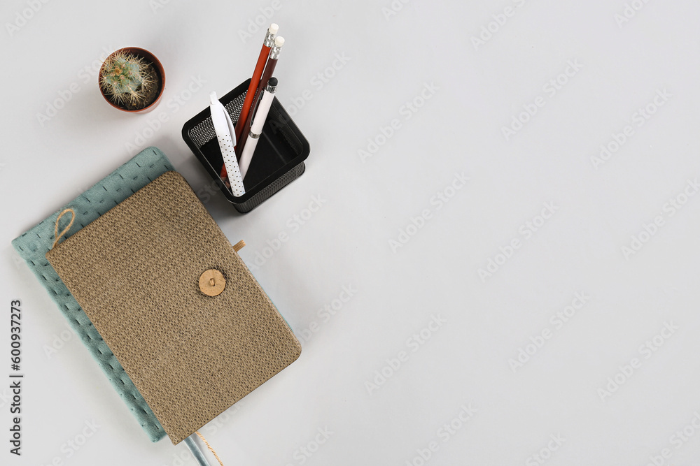 Stationery holder, notebooks and cactus on grey background