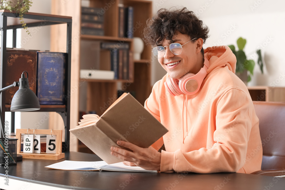 Male student reading book at table in library