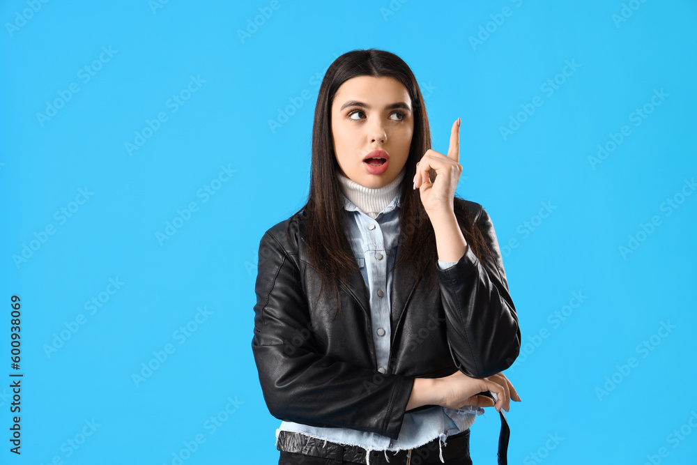 Thoughtful young woman with raised index finger on blue background