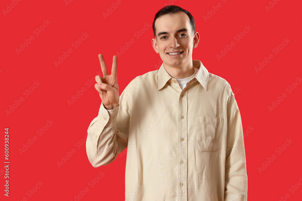 Young man showing two fingers on red background