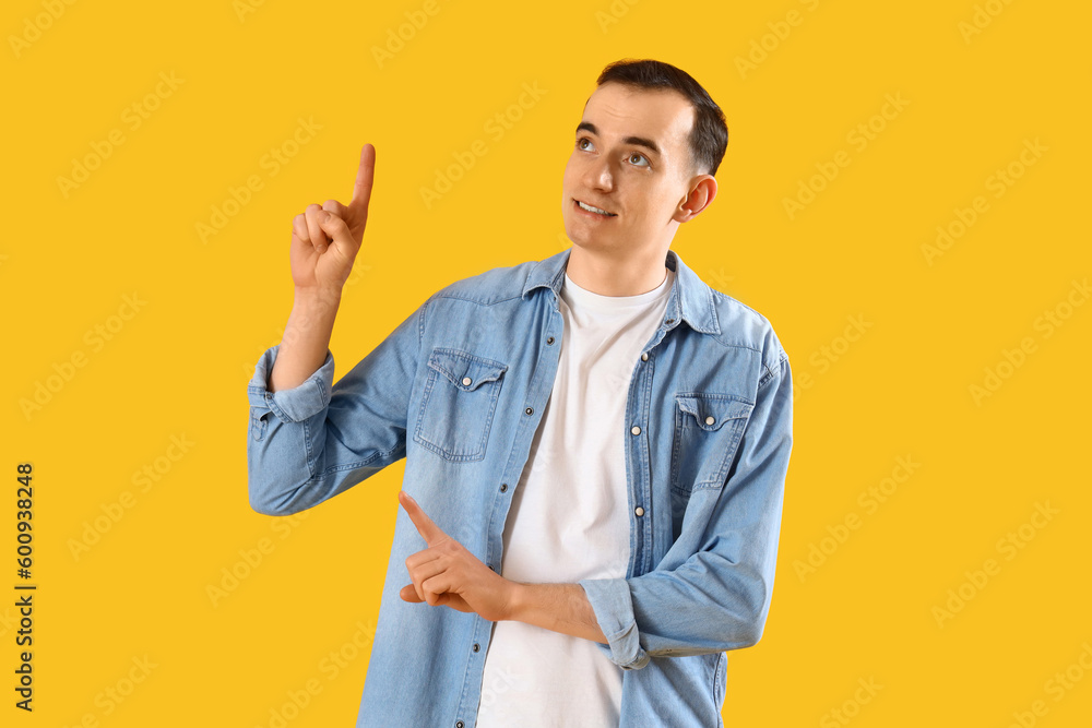 Young man pointing at something on yellow background