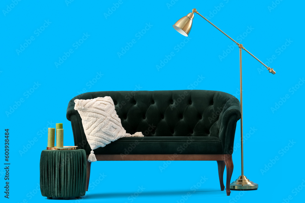 Cozy green sofa with cushion and pouf on blue background