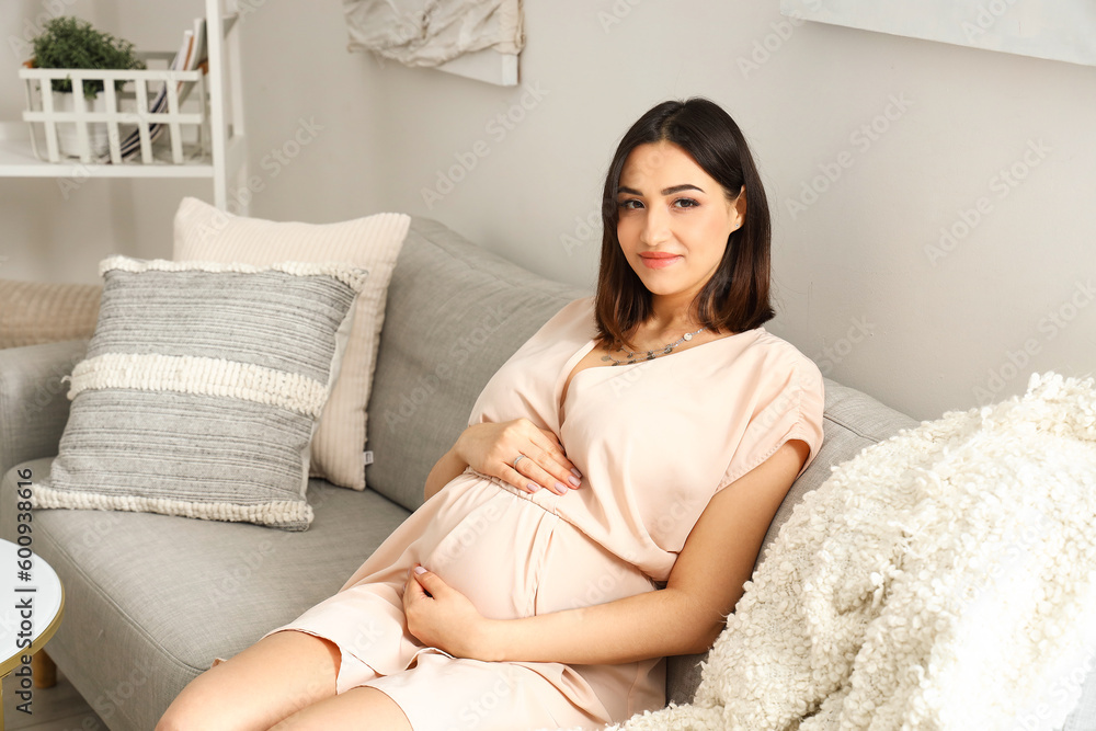 Young pregnant woman sitting on sofa at home