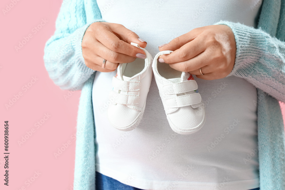 Young pregnant woman with baby booties on pink background, closeup