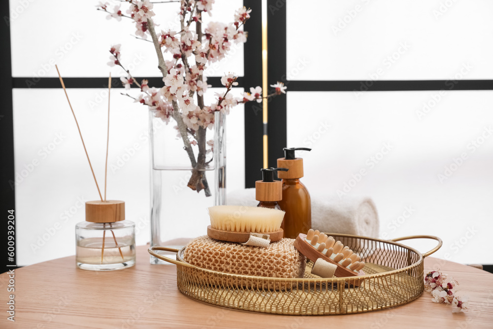 Vase with blooming branches and bath accessories on table in room