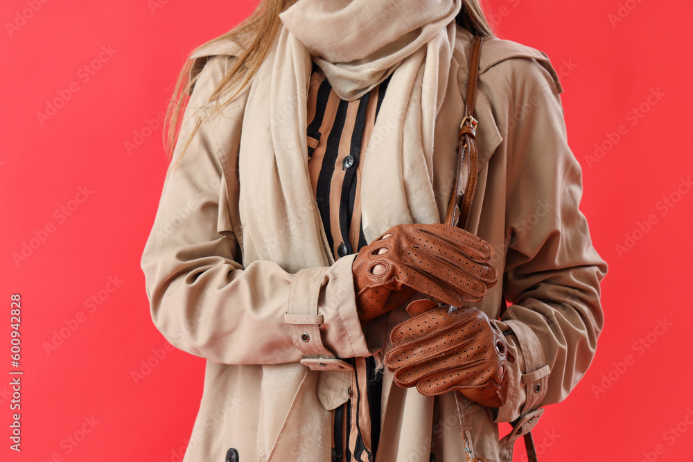 Beautiful young woman wearing leather gloves and coat on red background, closeup