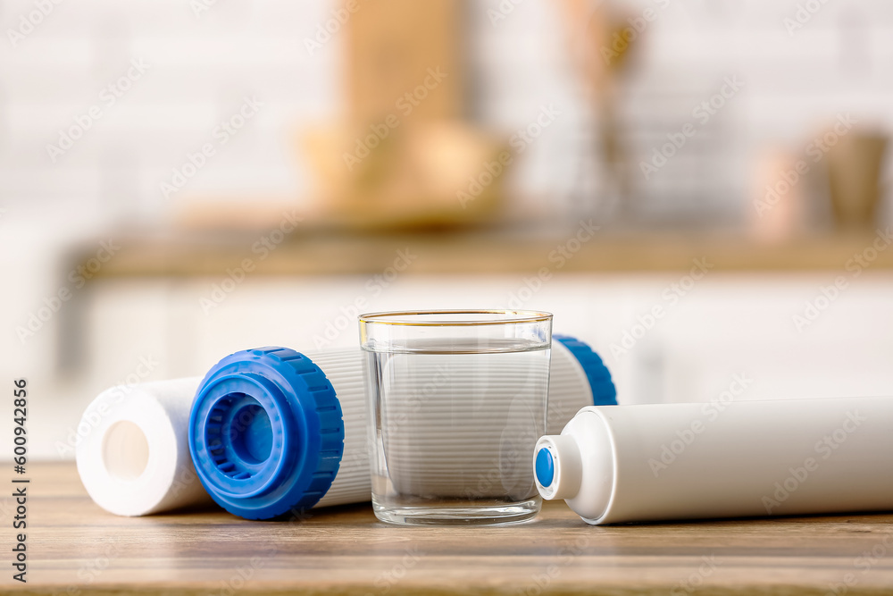 Glass of water with filters on wooden table in kitchen