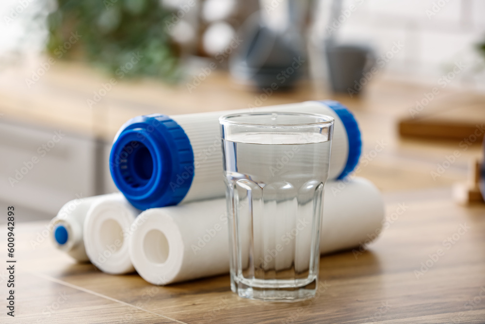 Glass of water with filters on wooden table in kitchen