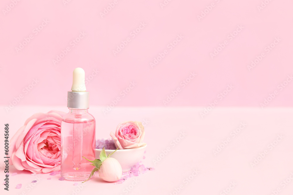 Bottle of cosmetic oil with rose extract and flowers on pink background