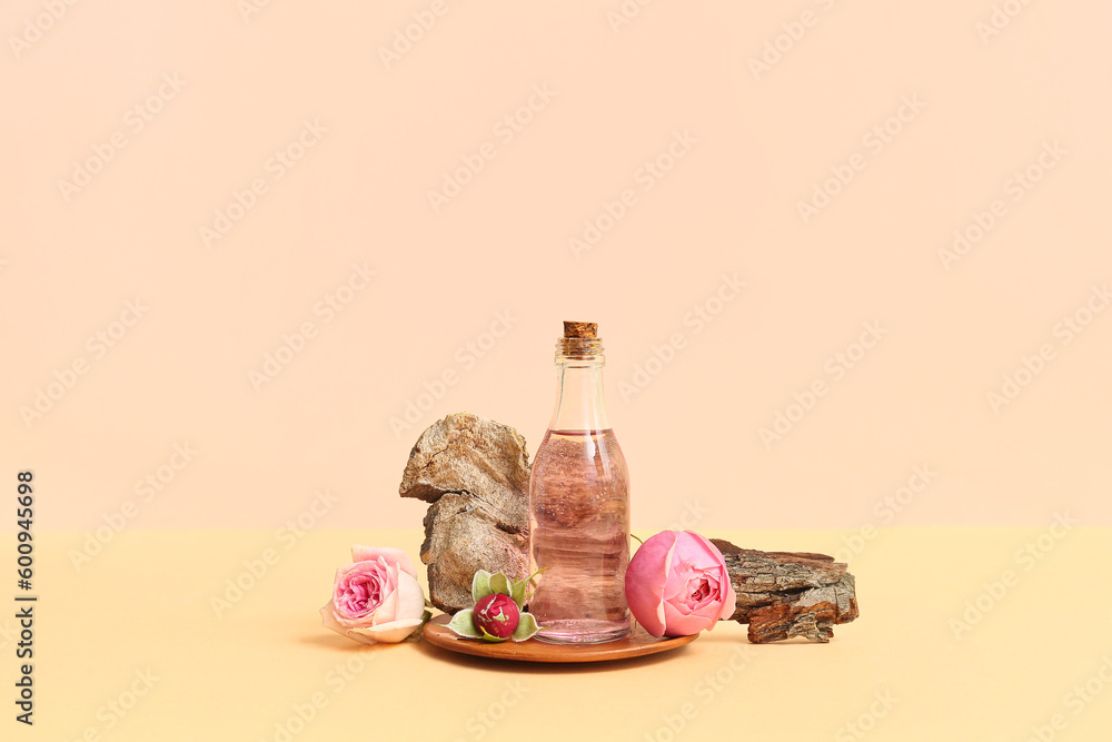 Bottle of cosmetic oil with rose extract and flowers on beige background