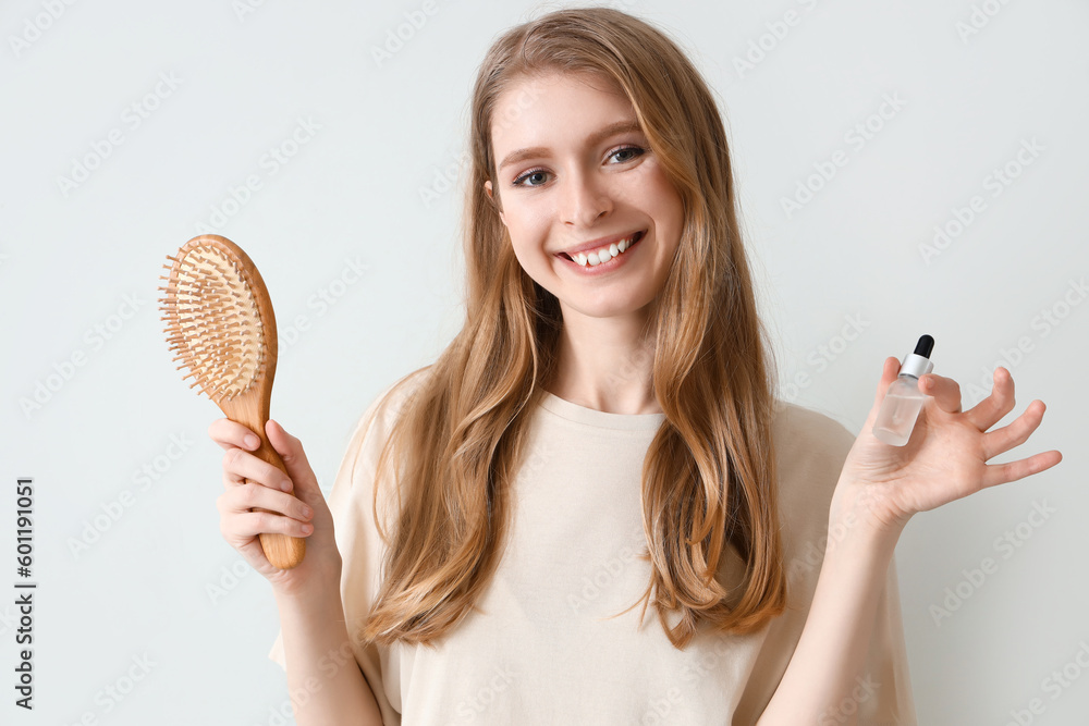 Young woman with serum for hair growth and brush on light background