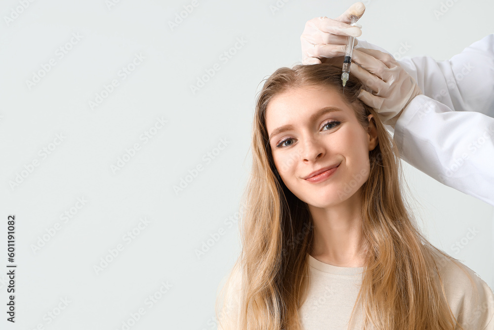 Young woman with hair loss problem receiving injection on light background