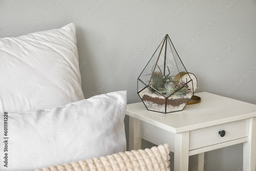 Florarium with alarm clock on table in light bedroom