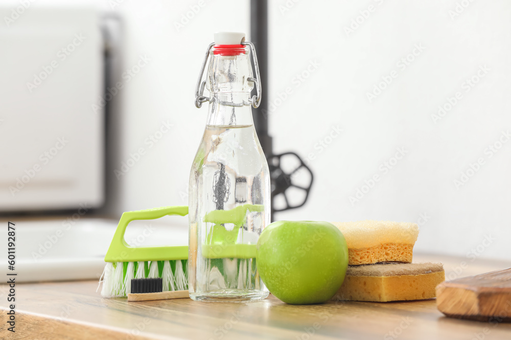 Bottle of vinegar, brushes, sponges and apple on wooden table