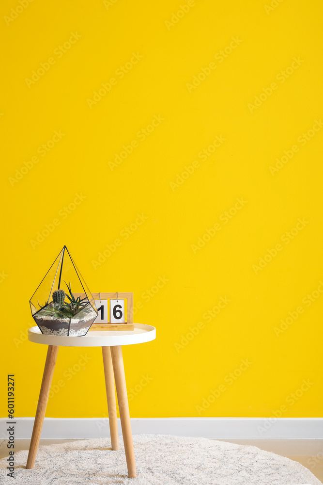 Florarium with calendar on table near yellow wall in room