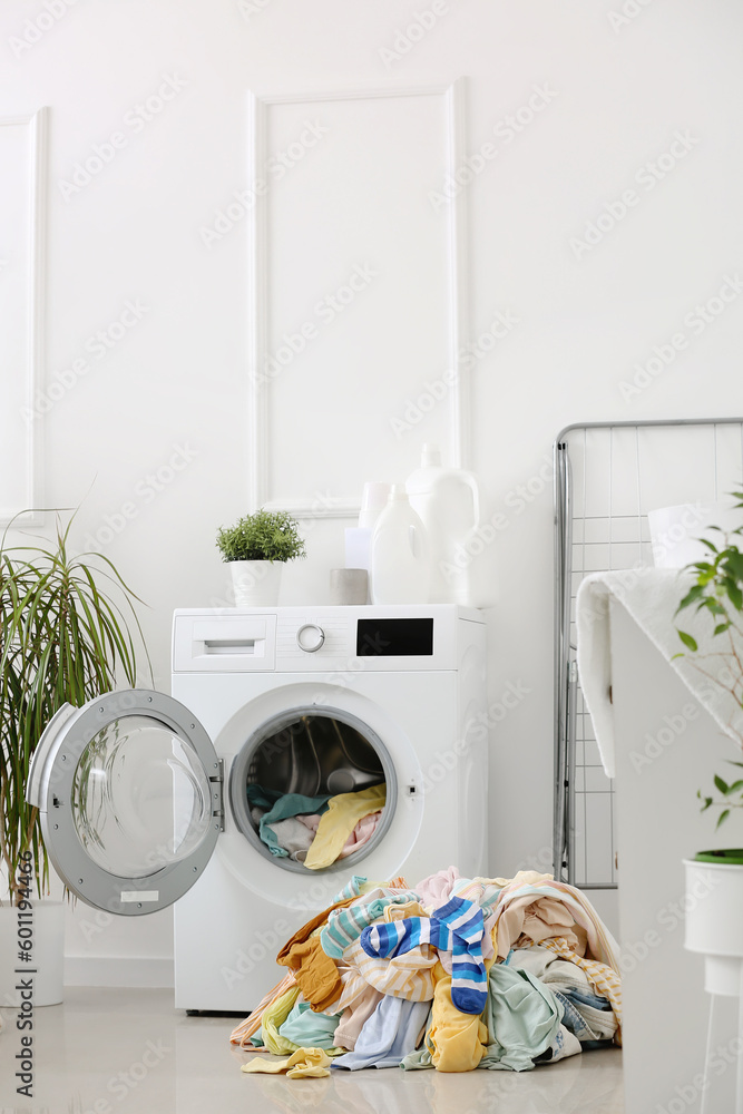 Stack of dirty clothes and washing machine in laundry room