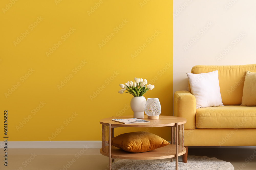 Cozy armchair and coffee table with tulip flowers in vase near colorful wall