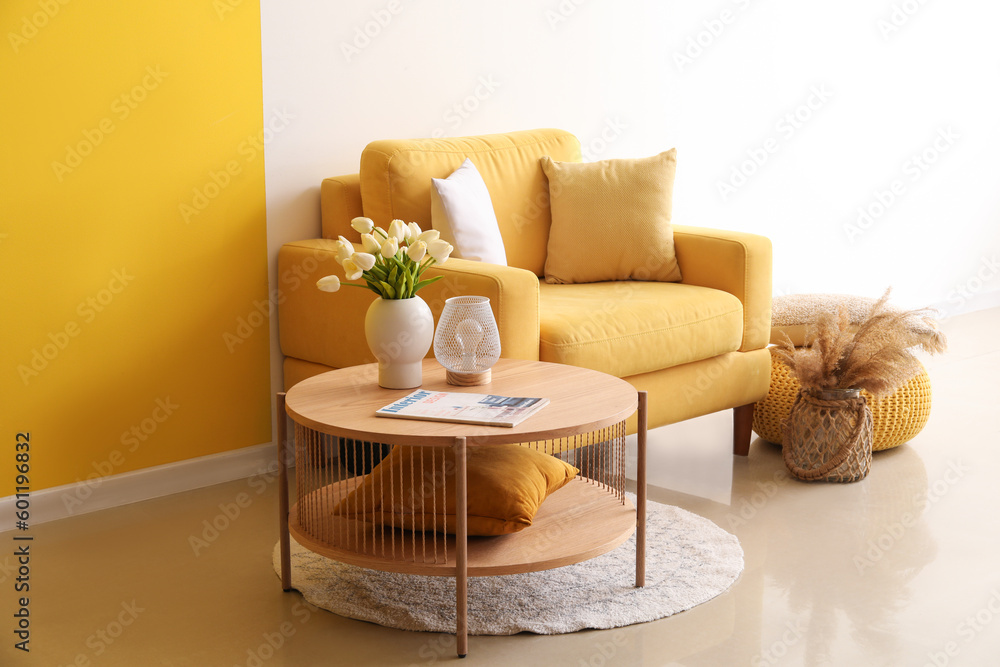 Cozy armchair and coffee table with tulip flowers in vase near colorful wall