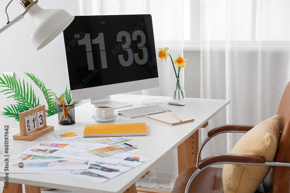 Comfortable designers workplace with modern PC and beautiful narcissus flowers near window