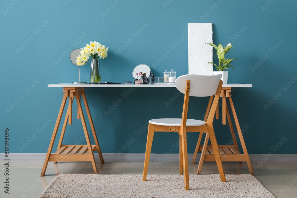 Table with different cosmetics and narcissus flowers near blue wall