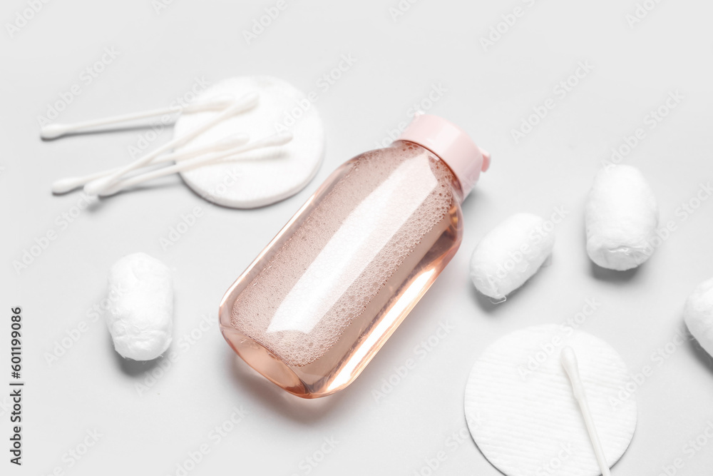 Bottle of micellar water with cotton balls, buds and pads on light background, closeup