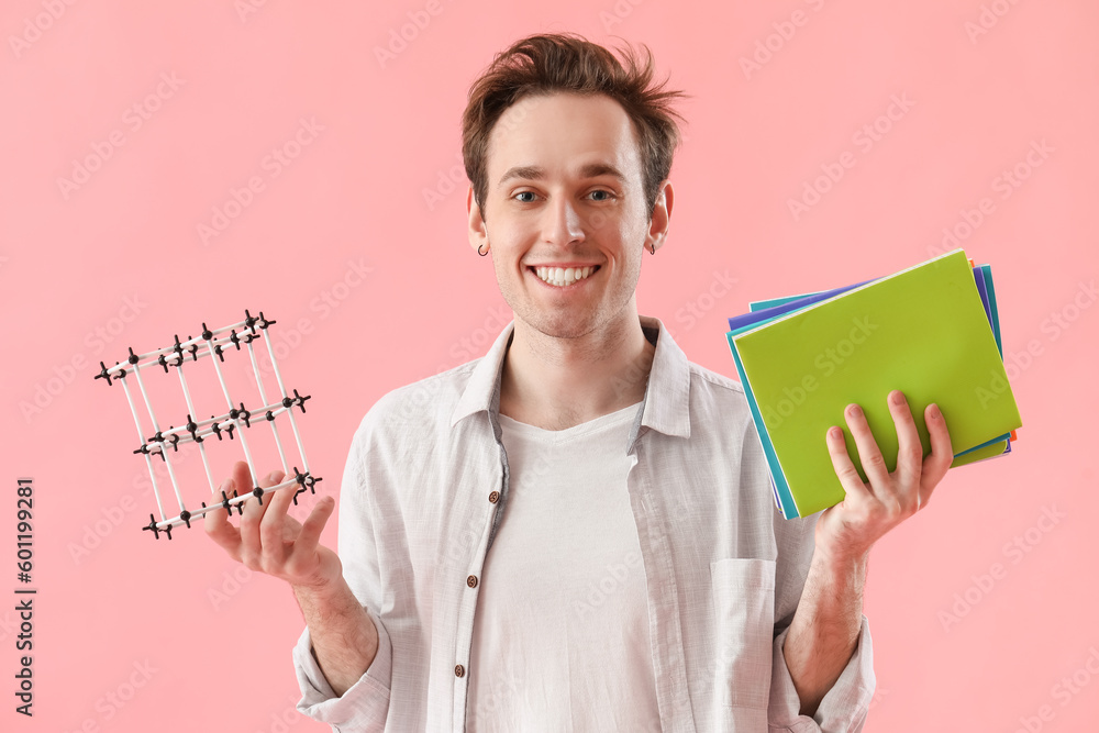 Male student with notebooks and model of crystal lattice on pink background