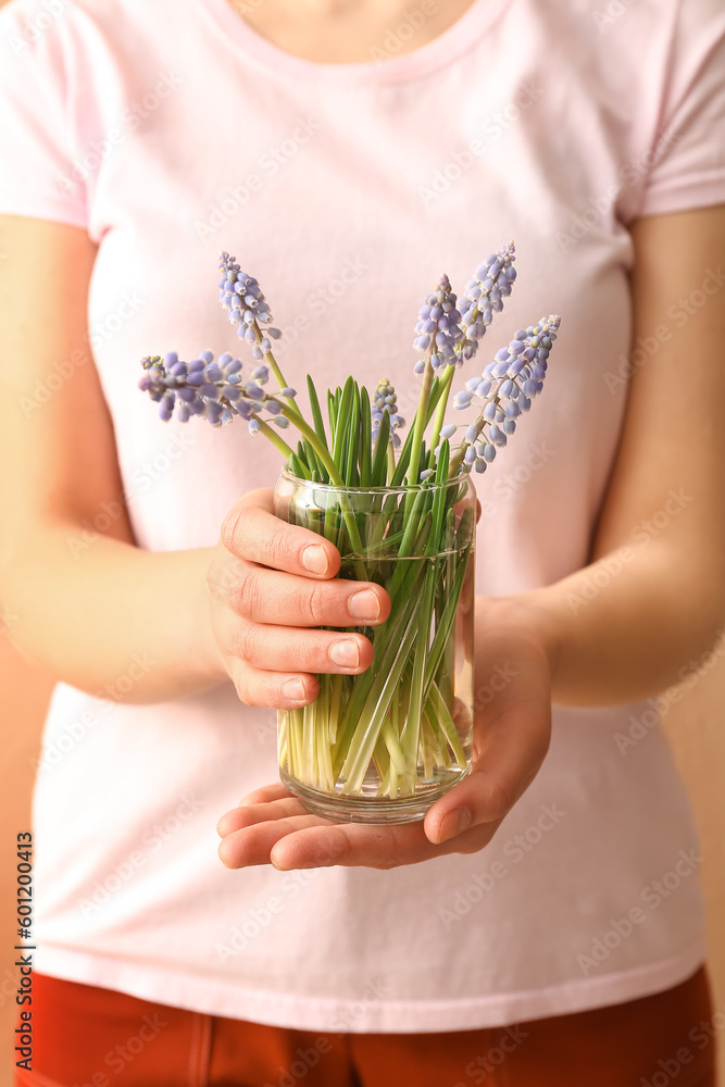 Woman holding glass with beautiful Muscari flowers on beige background