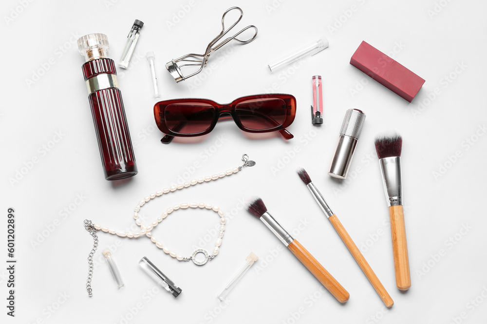 Sunglasses with perfume, jewelry and makeup brushes on white background