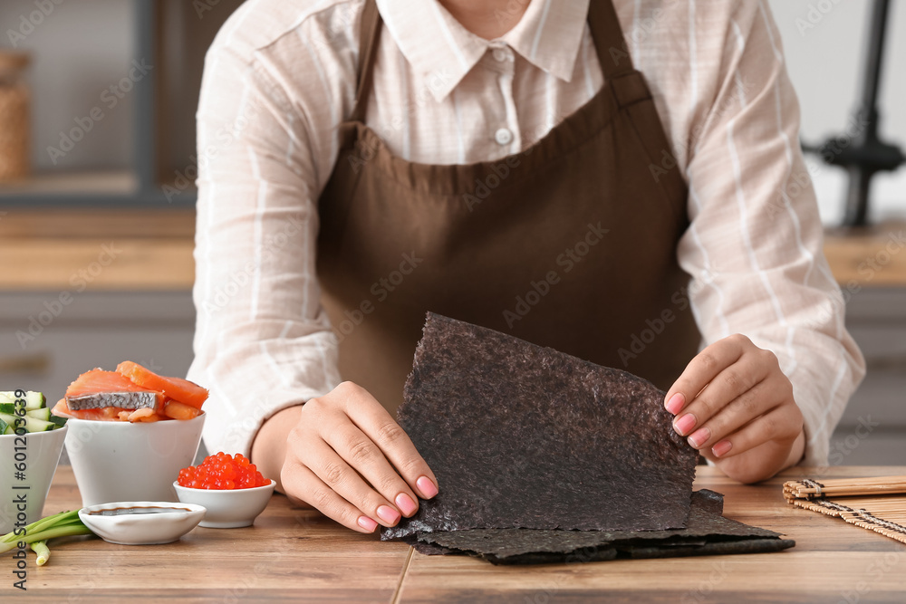 Woman preparing delicious sushi rolls in kitchen