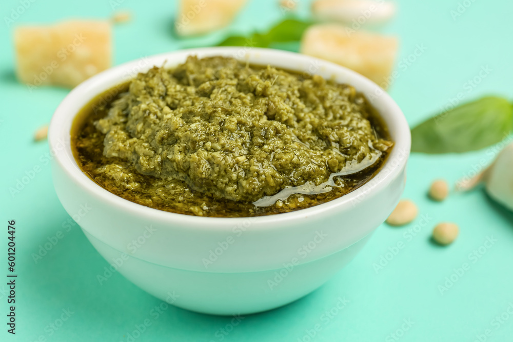 Bowl of delicious pesto sauce on turquoise background, closeup