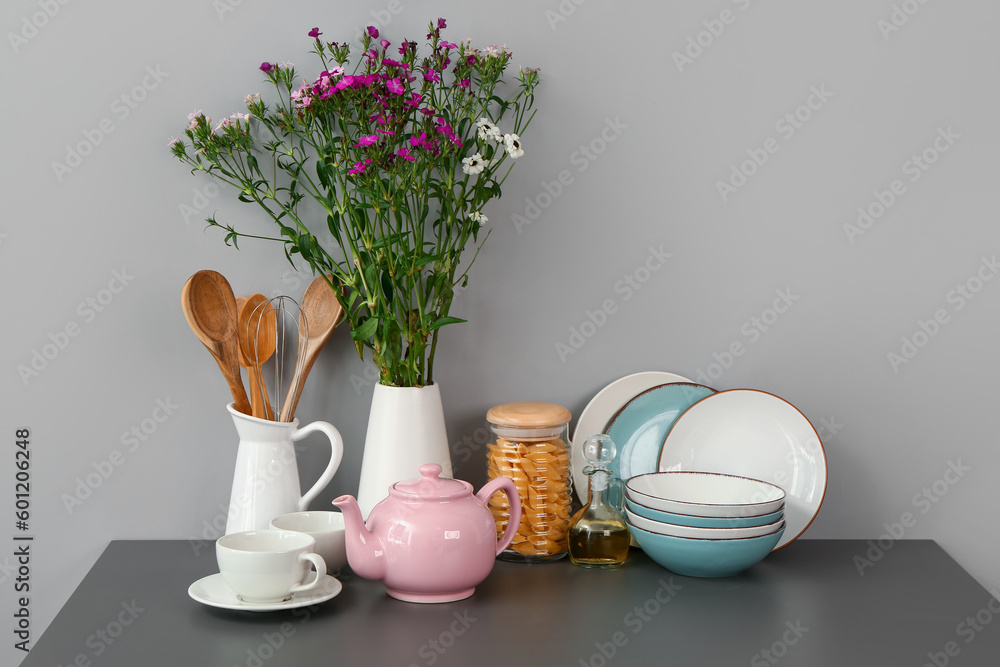 Composition with tea set, flowers and different kitchen stuff on black table