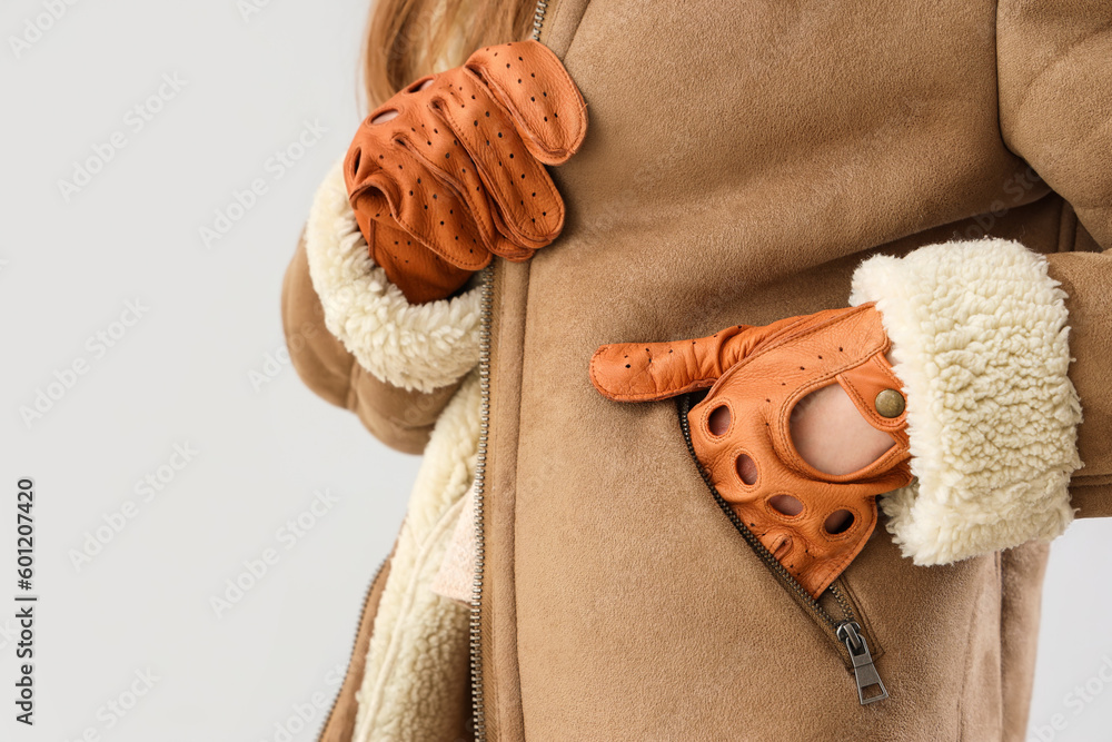 Beautiful young woman in leather gloves and sheepskin on light background, closeup