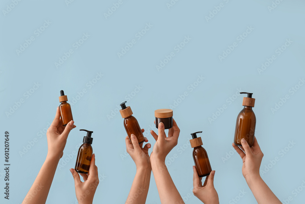 Hands holding different cosmetic products on light blue background