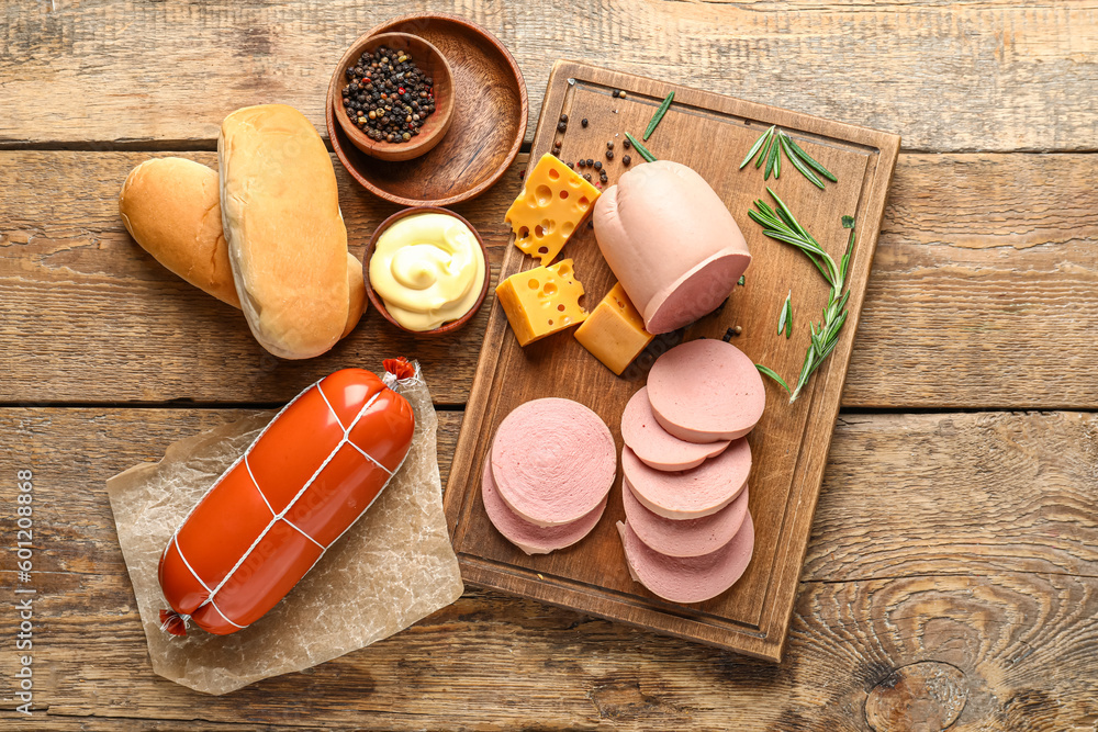 Board with tasty boiled sausages, cheese, sauce and bread on wooden background