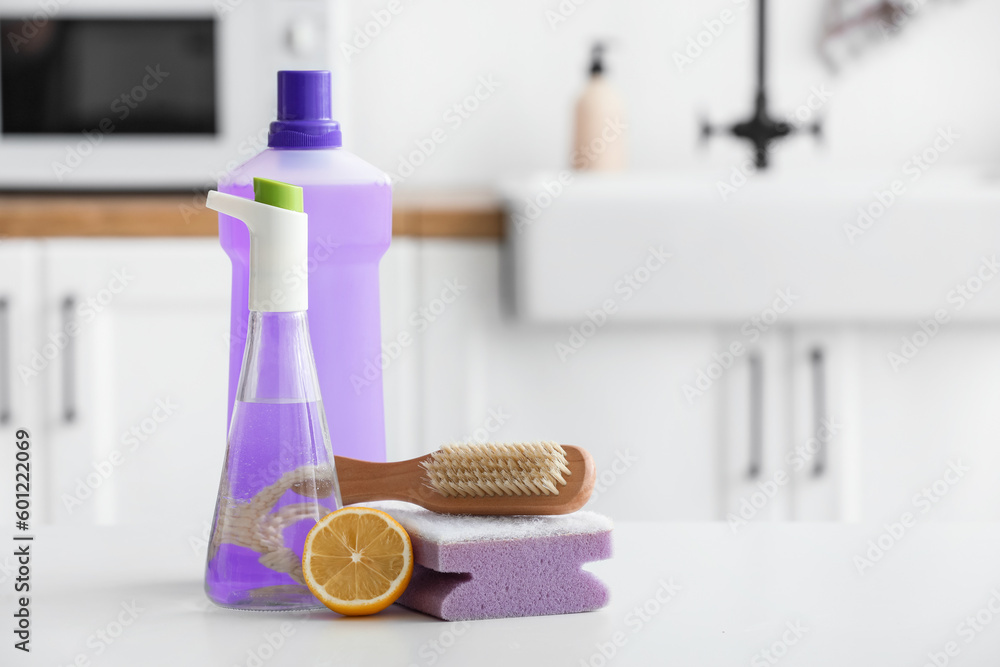 Bottles of vinegar, detergent, sponge, brush and lemon on table in  kitchen