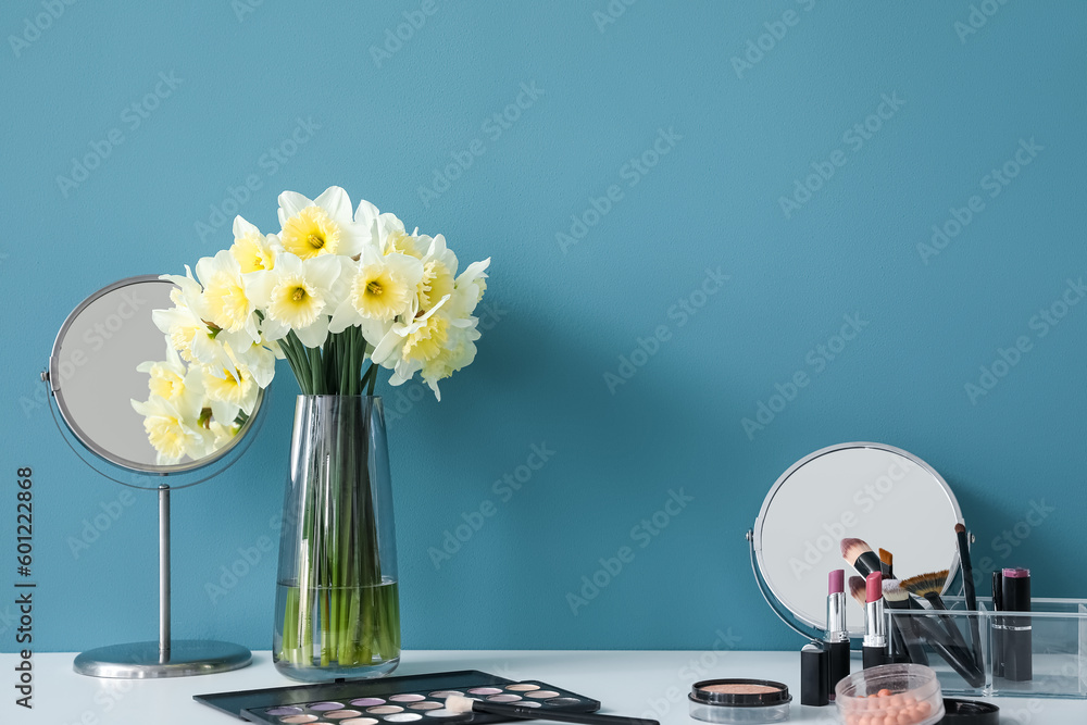 Table with different cosmetics and narcissus flowers near blue wall